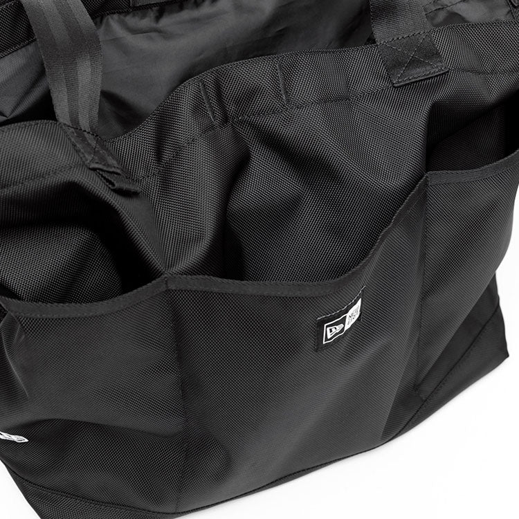 Top view close-up of a black New Era gym tote bag showing its open main compartment, multiple exterior slip pockets, and top carry straps.