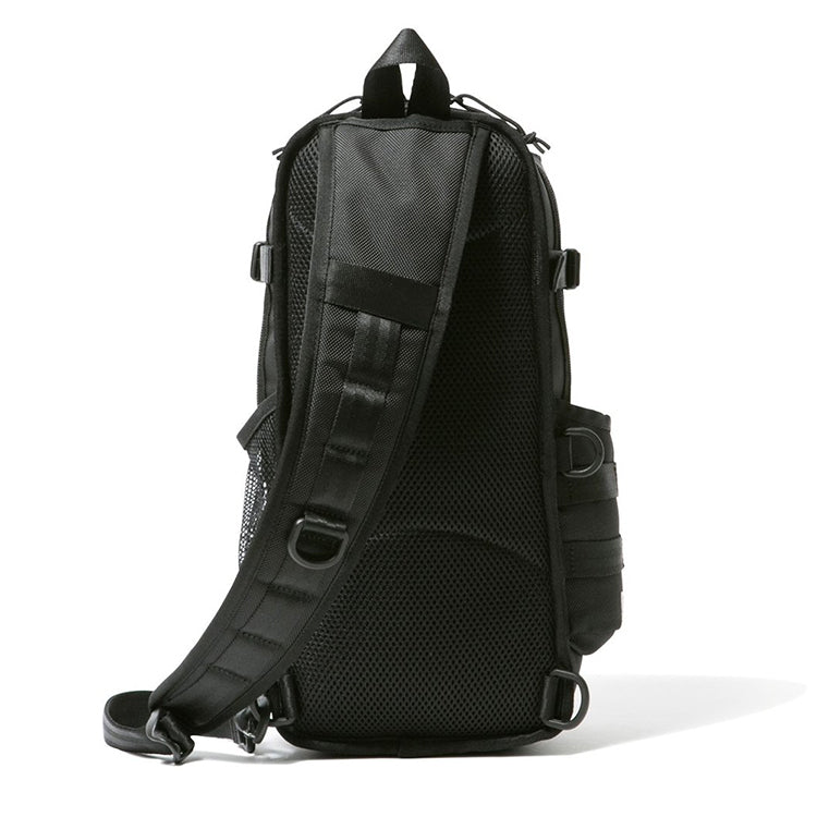 Rear view of a black tactical sling backpack with a padded shoulder strap, mesh back panel, D-rings, and side pockets.