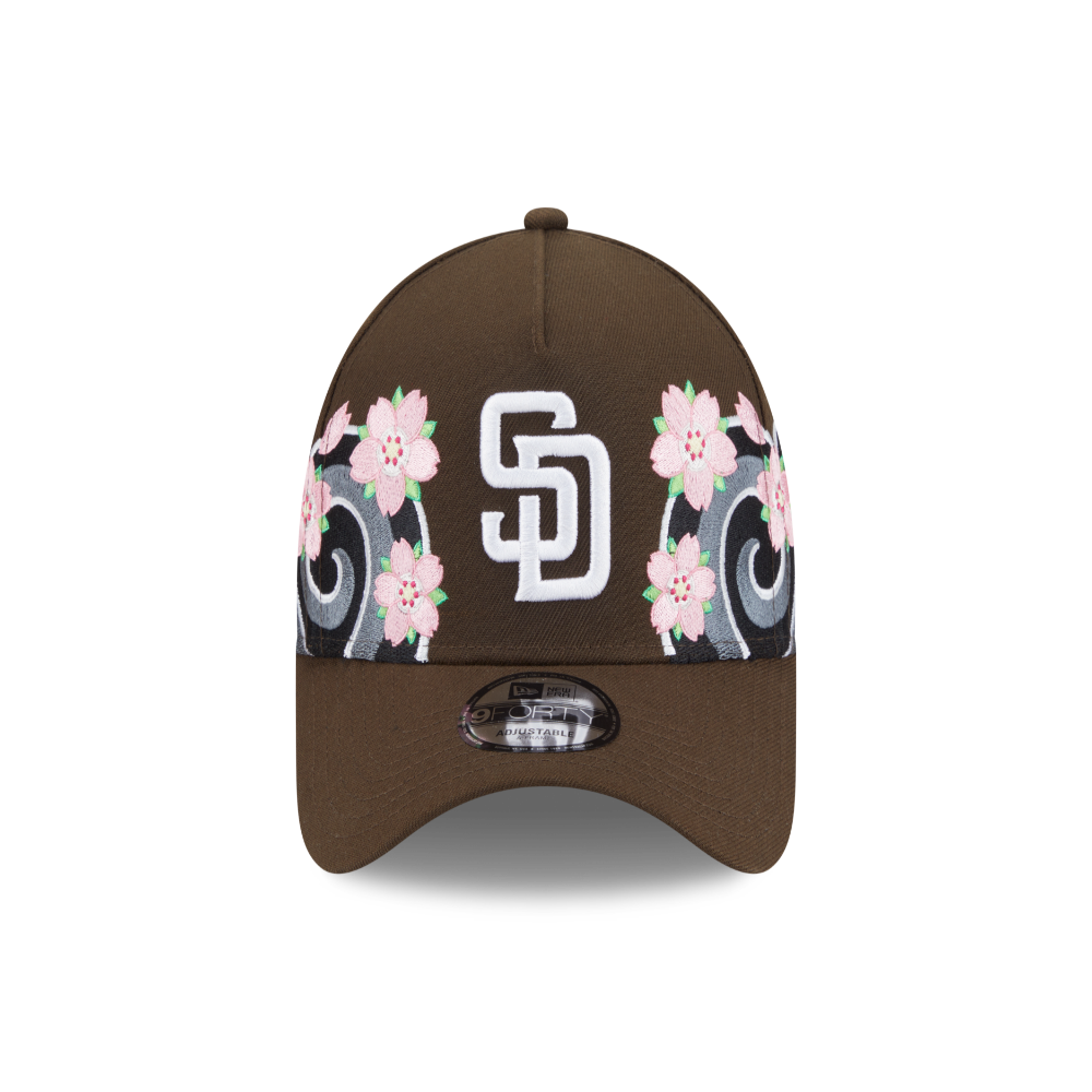 A brown baseball cap featuring a white interlocking 'SD' logo on the front, flanked by pink cherry blossom flowers and gray scrollwork on a black band, with a New Era 9FIFTY sticker on the brim.