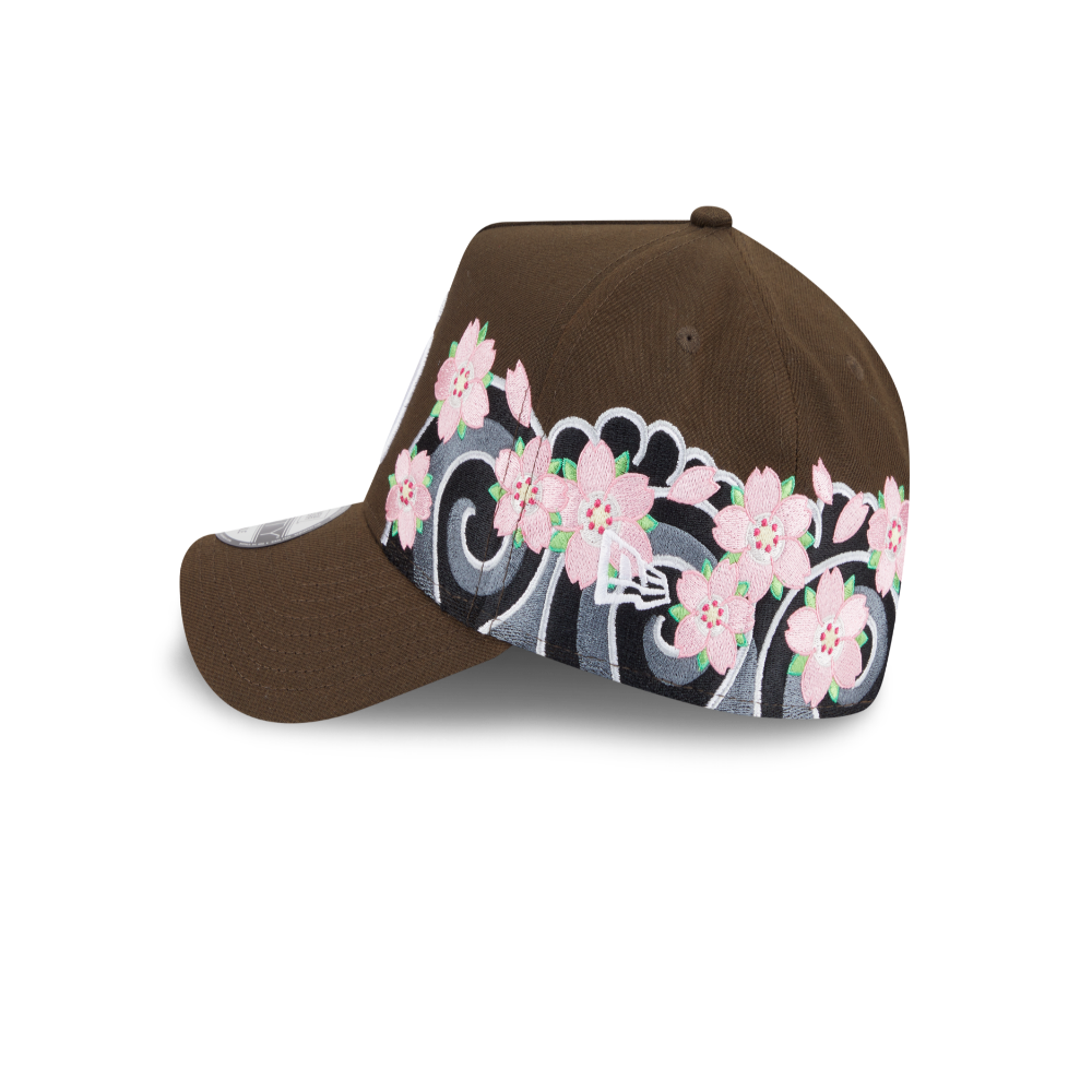 A brown baseball cap featuring a decorative band of pink cherry blossom flowers and gray scrollwork on the side panels, with a small white embroidered New Era logo.