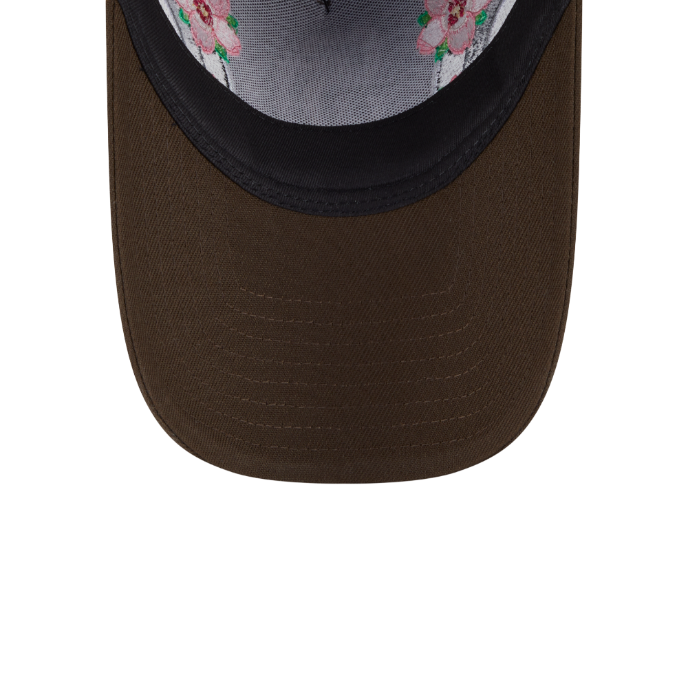 Close-up of the front of a trucker-style cap showing a dark brown curved brim, black embroidered front band, and a gray mesh back with pink floral embroidery.