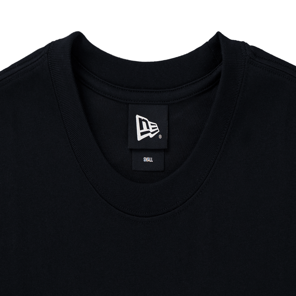 Close-up of a black crewneck t-shirt showing the inner neck label with the New Era logo and 'DRILL' text, on a solid white background.