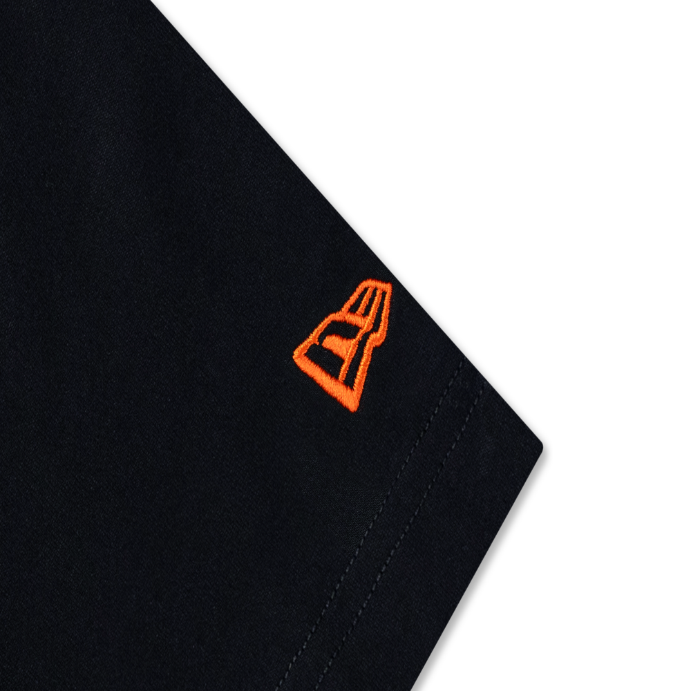 Close-up of a black fabric product corner with a small bright orange embroidered logo on a white background.