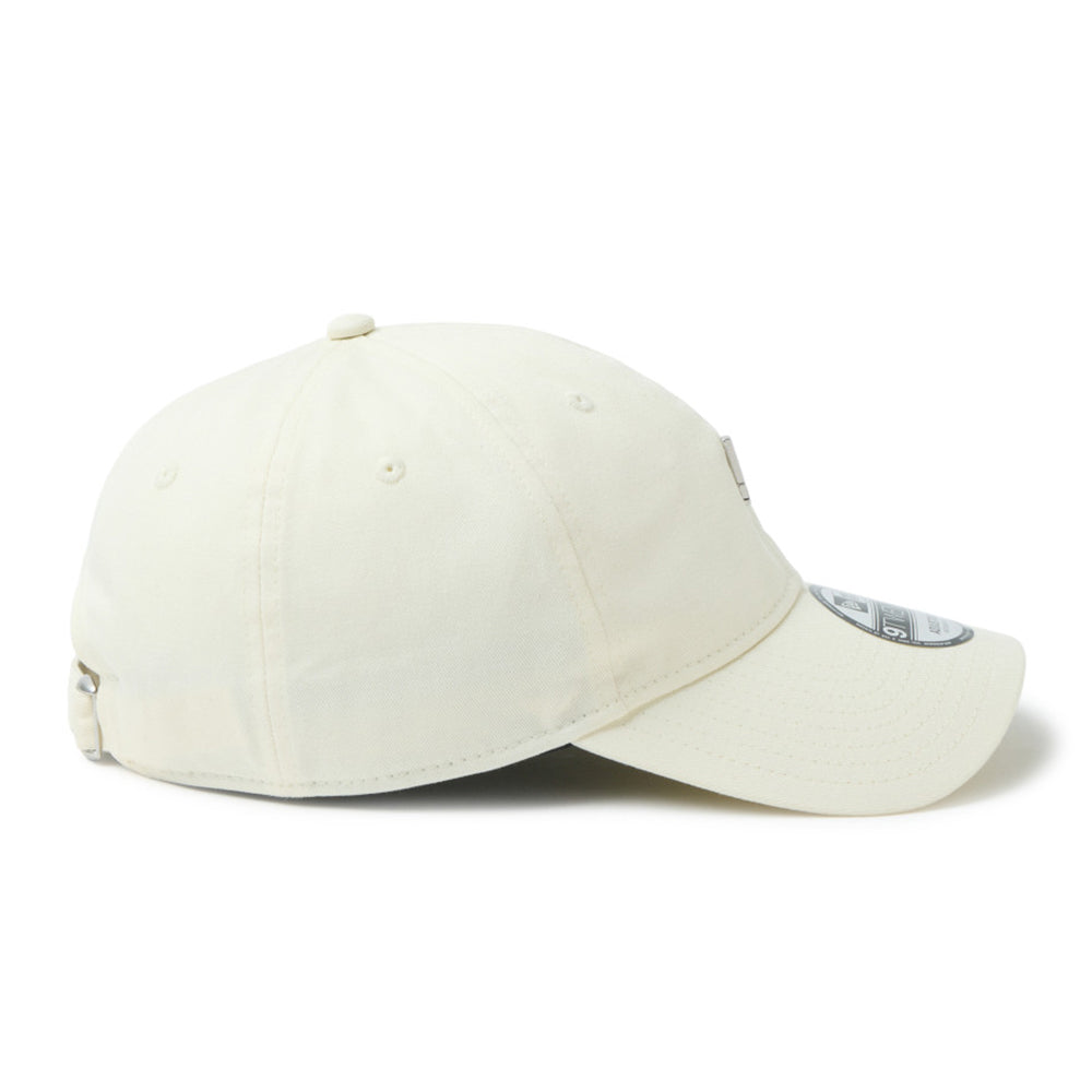 An off-white cotton baseball new era script mini metal logo cream 9twenty adjustable cap side shown from a three-quarters angle on a white background.