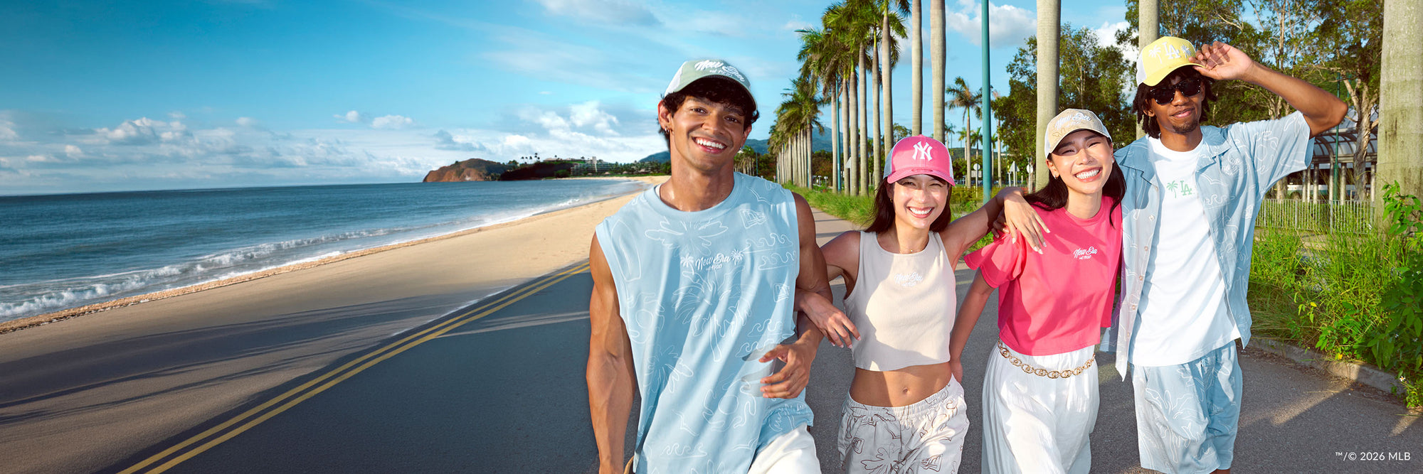 Four people walking along a beach road with palm trees and ocean view