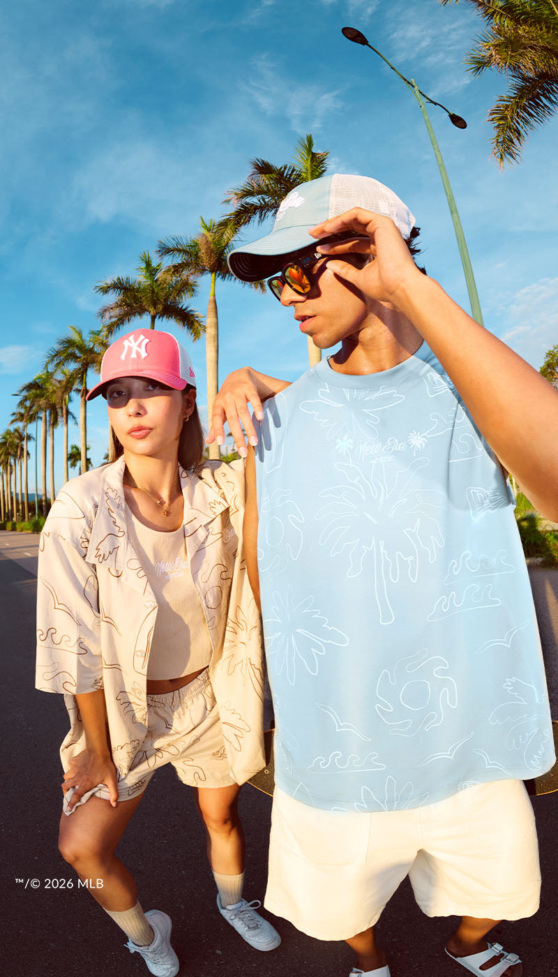 Two people standing outdoors with palm trees and a clear blue sky in the background.